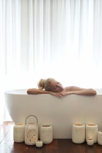 Woman lies in big white bath, candles are on the floor