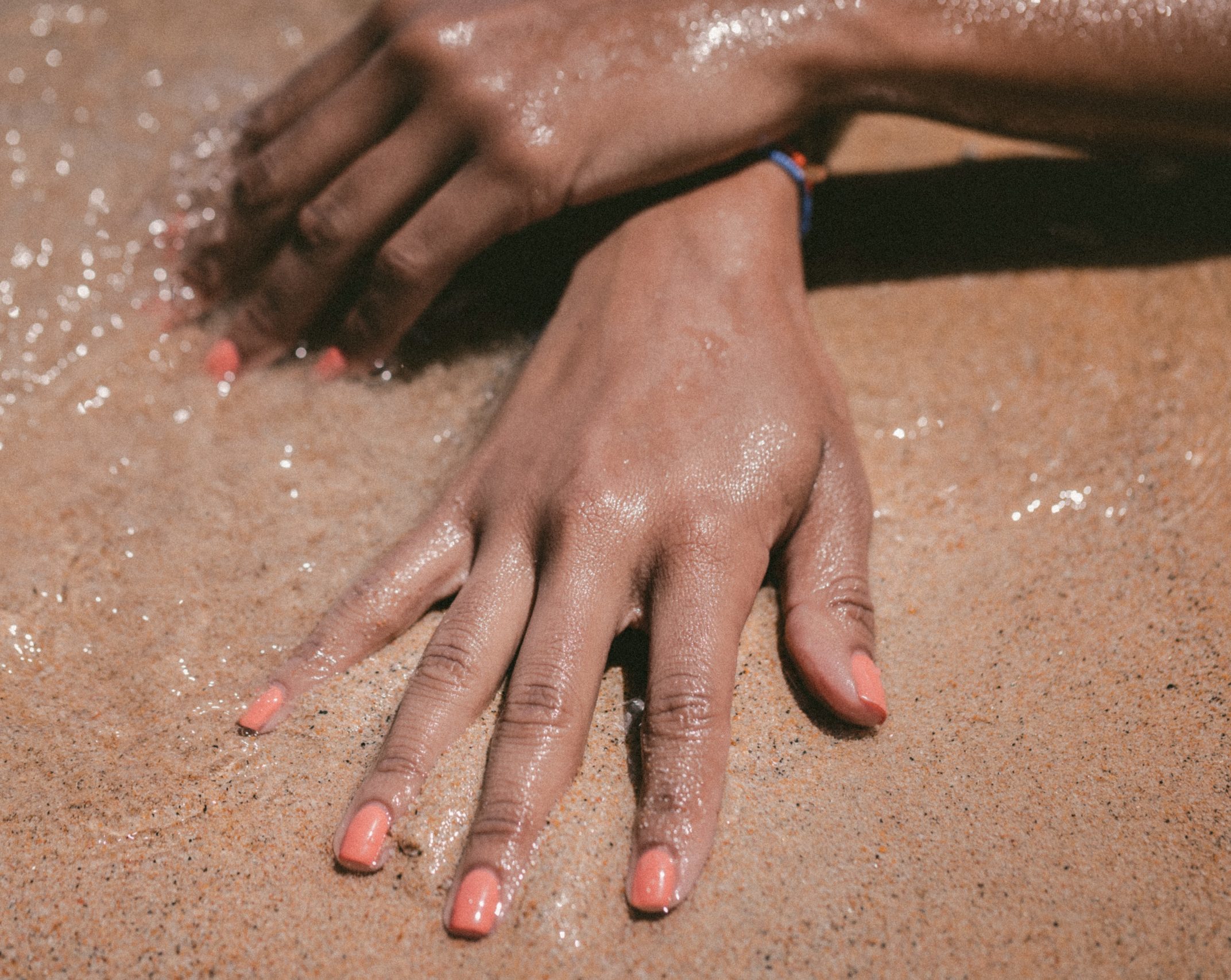 A pair of hands with pink nail polish lie on sand