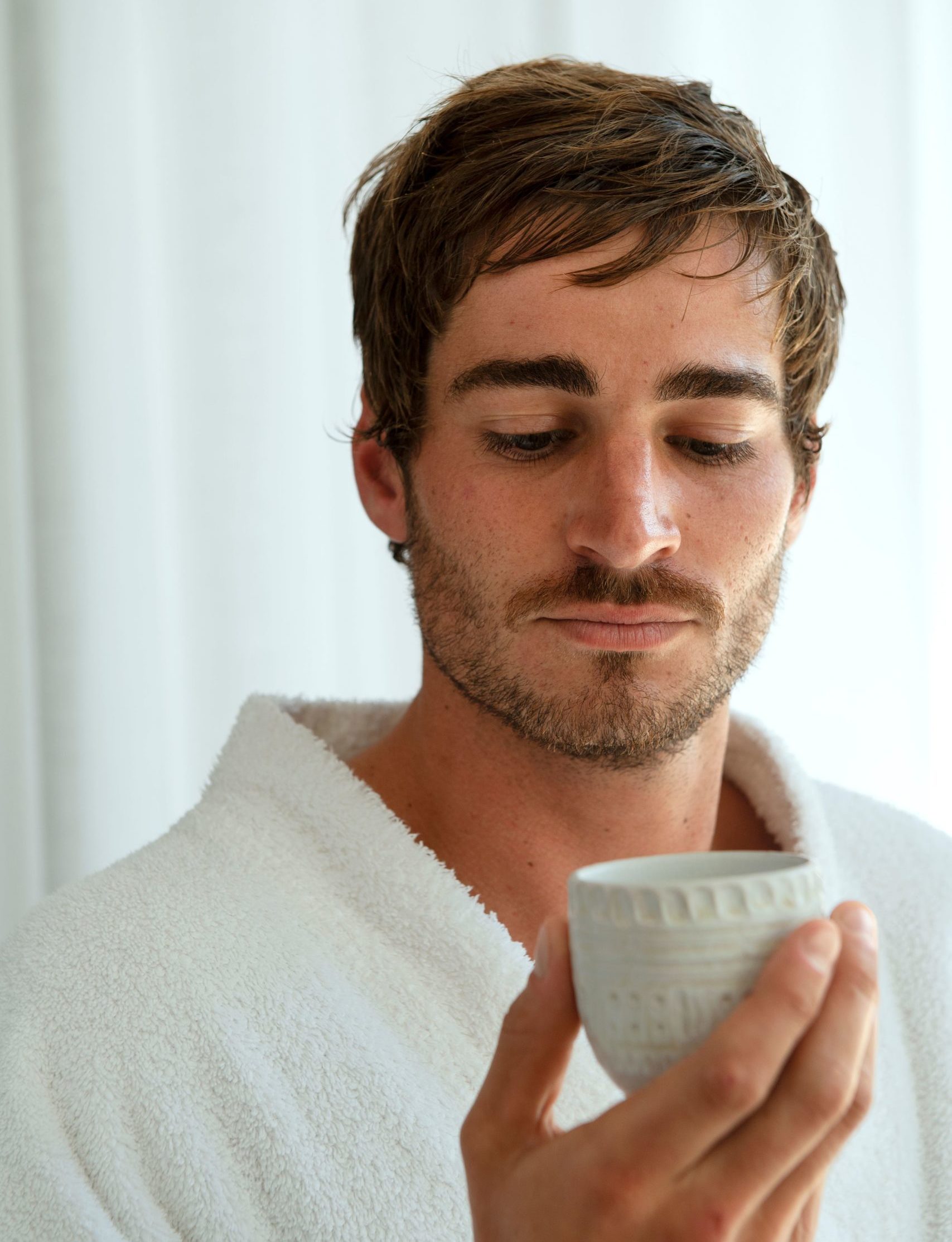 Upclose image of a man holding a cup of tea, wearing a bath robe